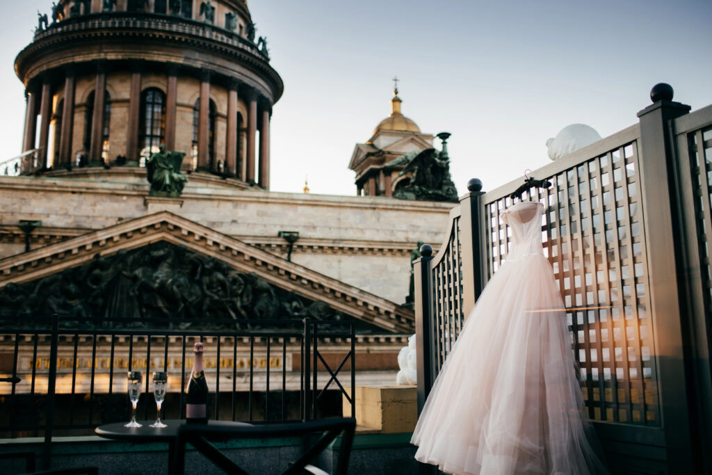 bridal gown hanging outside with wine on the table with two glasses.