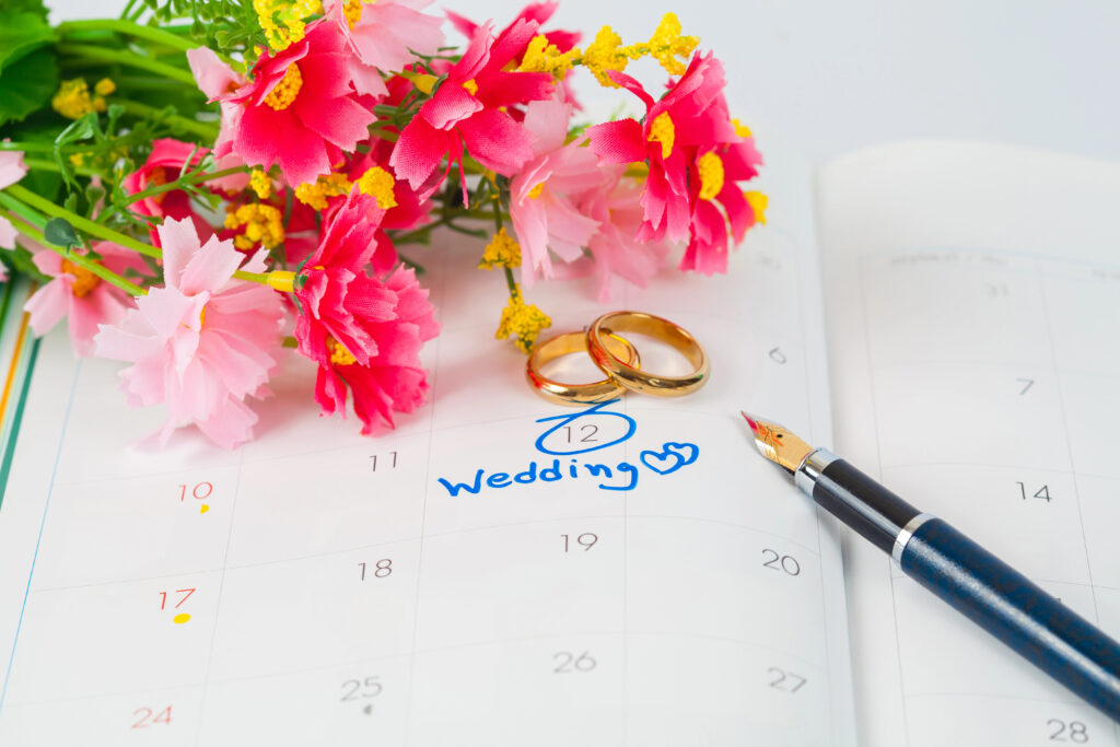 Calendar book with number 12 marked as wedding date with 2 wedding rings, flowers and a pen at the top.